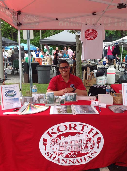 Man sitting and smiling at the Korth & Shannahan Painting booth at the Pleasantville Day